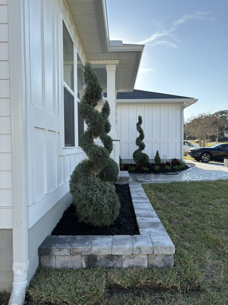 Curved landscape bed with stone edging and spiral topiary near home entry