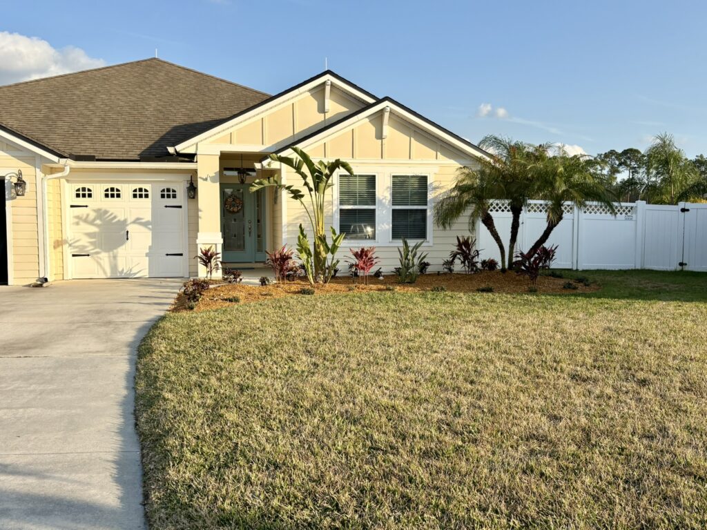 Front yard lawn with tropical landscape bed and palm trees near driveway